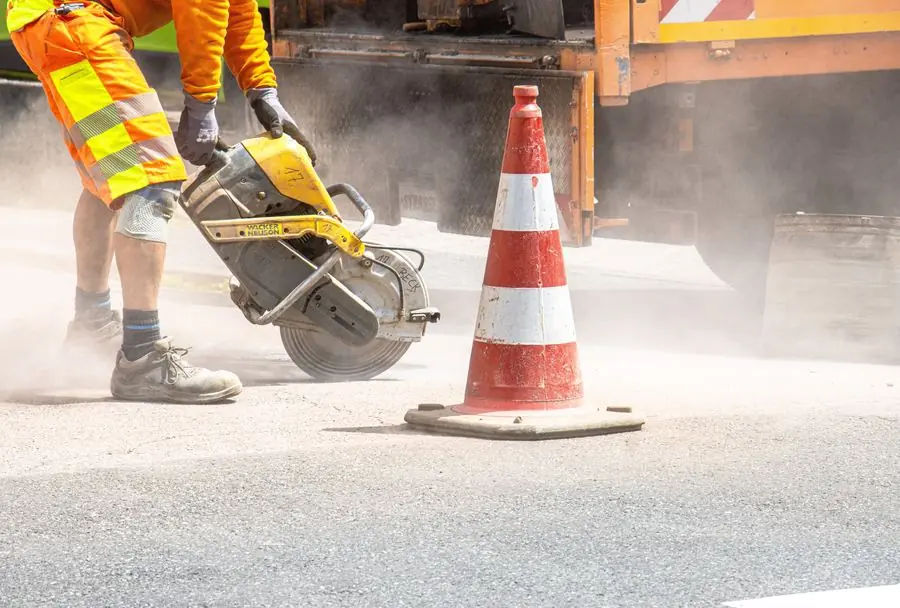 Operario cortando el borde del pavimento junto a un cono antes del bacheo con BACHEX: primer paso de la reparación